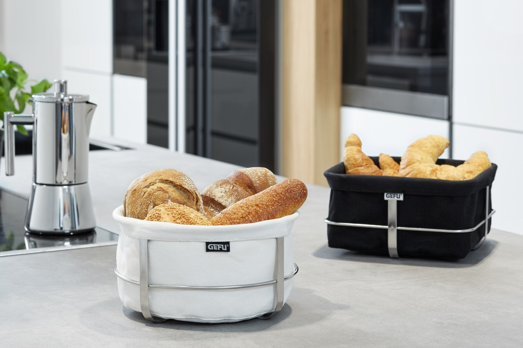 Virtuves galds ar balta auduma apaļu maizes grozu un melna auduma kvadrāta formas maizes grozu Gefu Brunch.